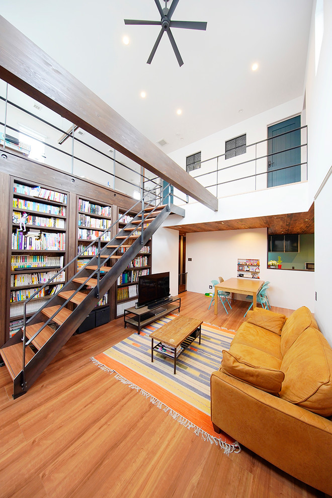 Cette photo montre un salon industriel ouvert avec une bibliothèque ou un coin lecture, un mur blanc, un sol en contreplaqué, aucune cheminée, un téléviseur indépendant et un sol marron.