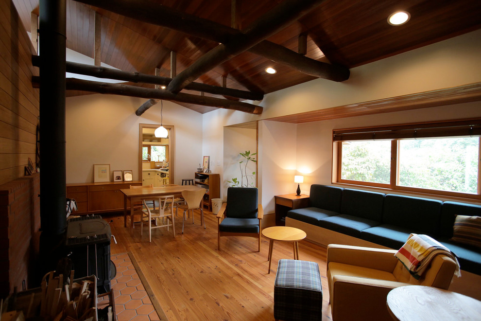 Idee per un soggiorno con pareti marroni, pavimento in legno massello medio, stufa a legna, cornice del camino in mattoni, pavimento marrone e soffitto in legno
