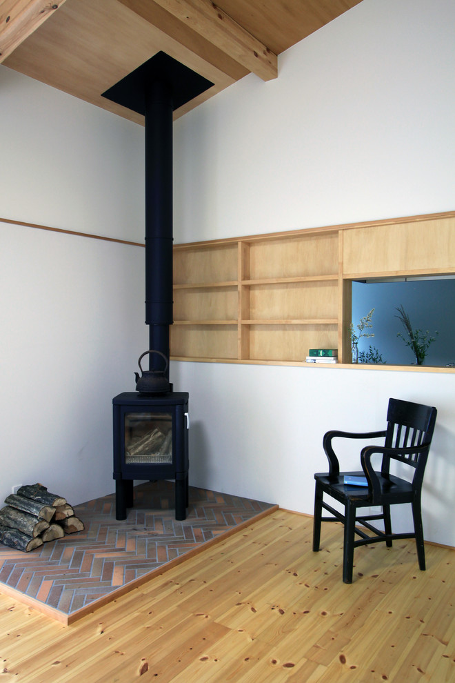 Cette image montre un salon asiatique ouvert avec un sol en bois brun, un poêle à bois et un manteau de cheminée en brique.