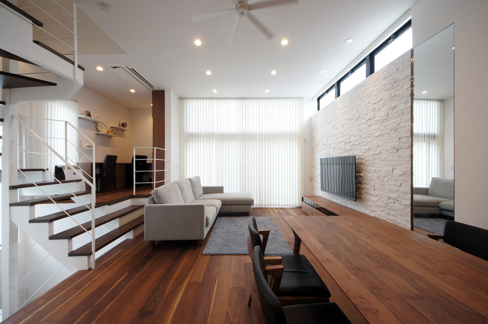 Modelo de salón abierto minimalista con paredes blancas, suelo de madera oscura, televisor colgado en la pared y suelo marrón