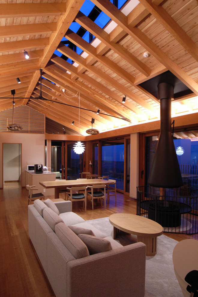 Aménagement d'un grand salon asiatique ouvert avec un mur blanc, cheminée suspendue, un sol marron et un sol en bois brun.