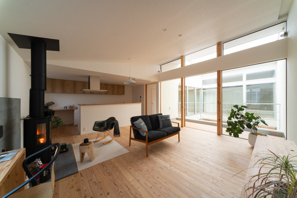 Idée de décoration pour un salon nordique ouvert avec un mur blanc, parquet clair, un poêle à bois, un manteau de cheminée en béton et un téléviseur indépendant.