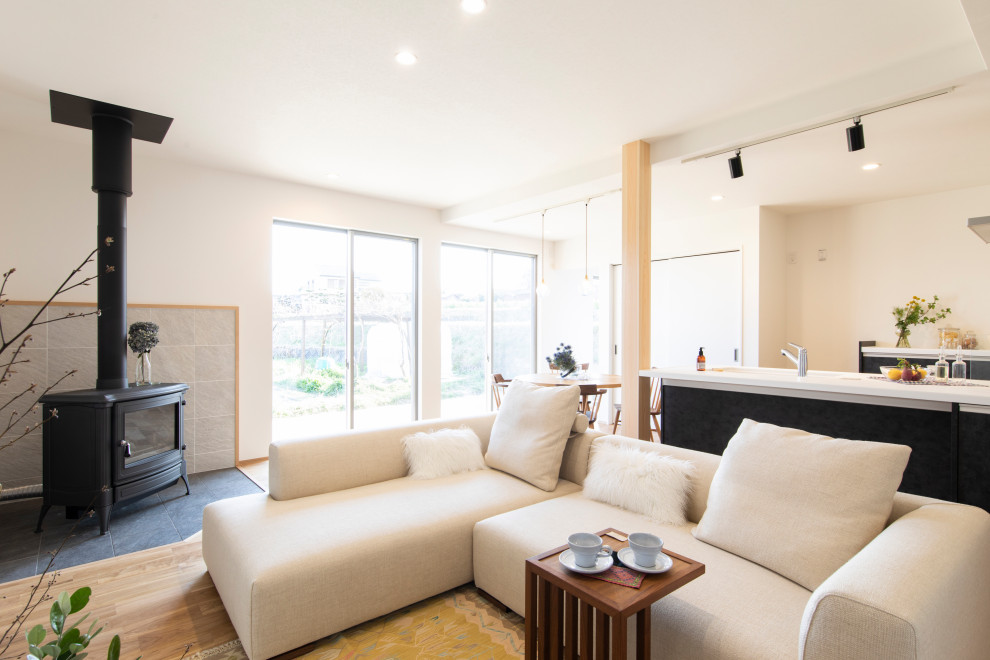 Modernes Wohnzimmer mit weißer Wandfarbe, braunem Holzboden, Kaminofen, gefliester Kaminumrandung, TV-Wand, grauem Boden und Tapetendecke in Sonstige