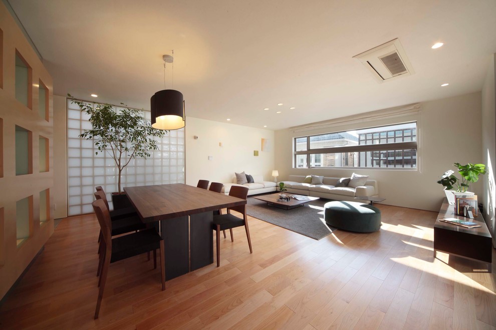 This is an example of a world-inspired living room in Tokyo with white walls, light hardwood flooring and brown floors.