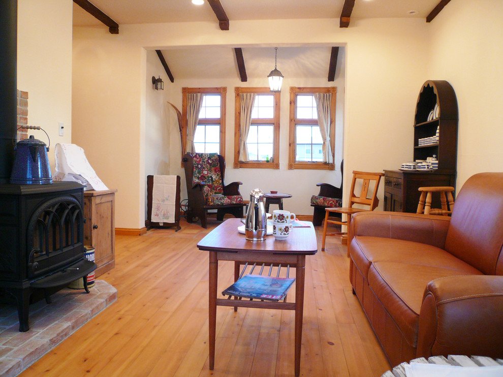 На фото: гостиная комната в стиле кантри с паркетным полом среднего тона, печью-буржуйкой, фасадом камина из кирпича, коричневым полом и белыми стенами с