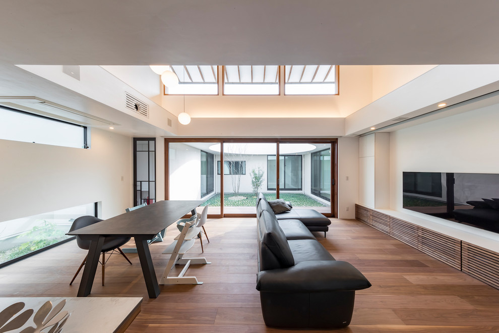 Immagine di un soggiorno moderno con pareti bianche, pavimento in legno massello medio, TV a parete e pavimento marrone
