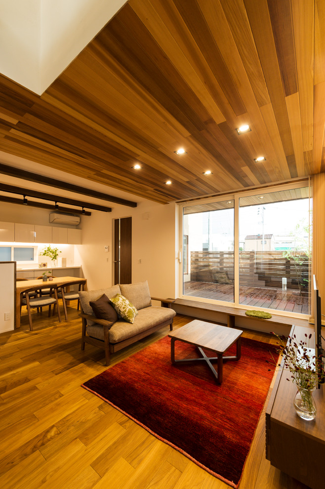 Cette image montre un salon asiatique ouvert avec un mur blanc, un sol en bois brun, un sol marron et un téléviseur indépendant.