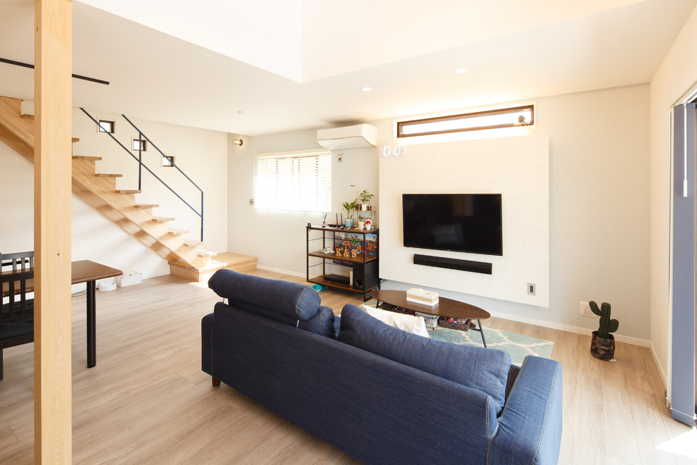 Идея дизайна: гостиная комната в стиле модернизм с белыми стенами, деревянным полом, телевизором на стене и бежевым полом