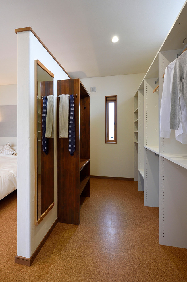 Example of a gender-neutral cork floor and brown floor walk-in closet design in Other with open cabinets and white cabinets