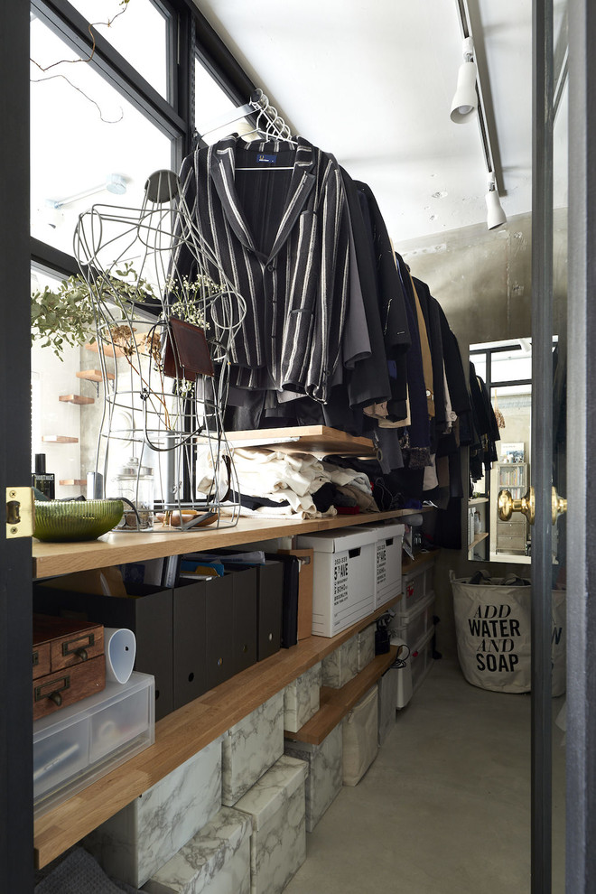 Inredning av ett industriellt walk-in-closet, med öppna hyllor, skåp i mellenmörkt trä, betonggolv och grått golv