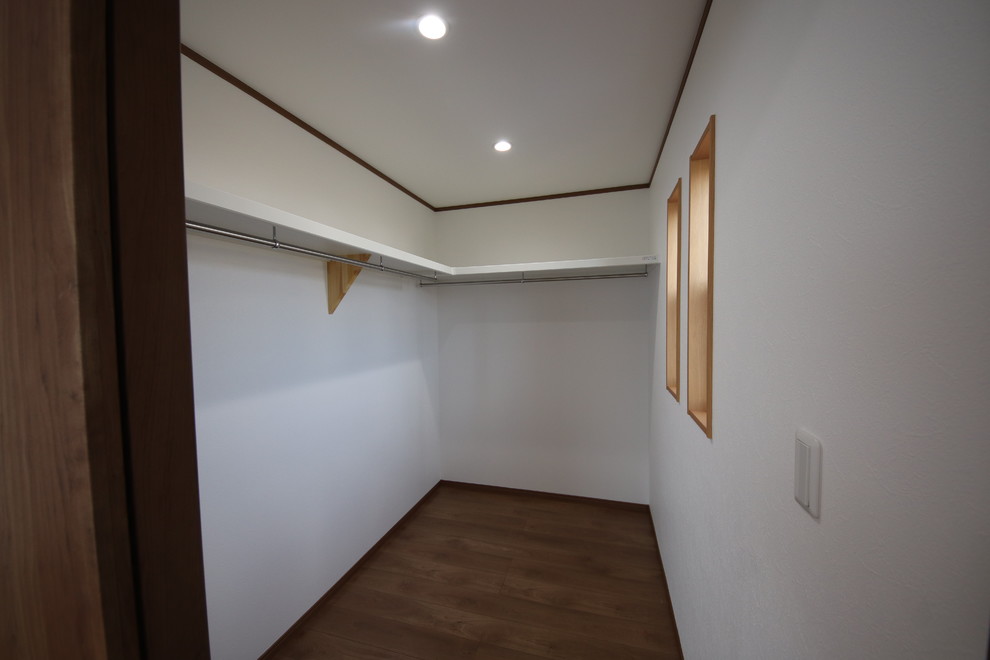 Immagine di una grande cabina armadio minimalista con pavimento in legno verniciato e pavimento marrone