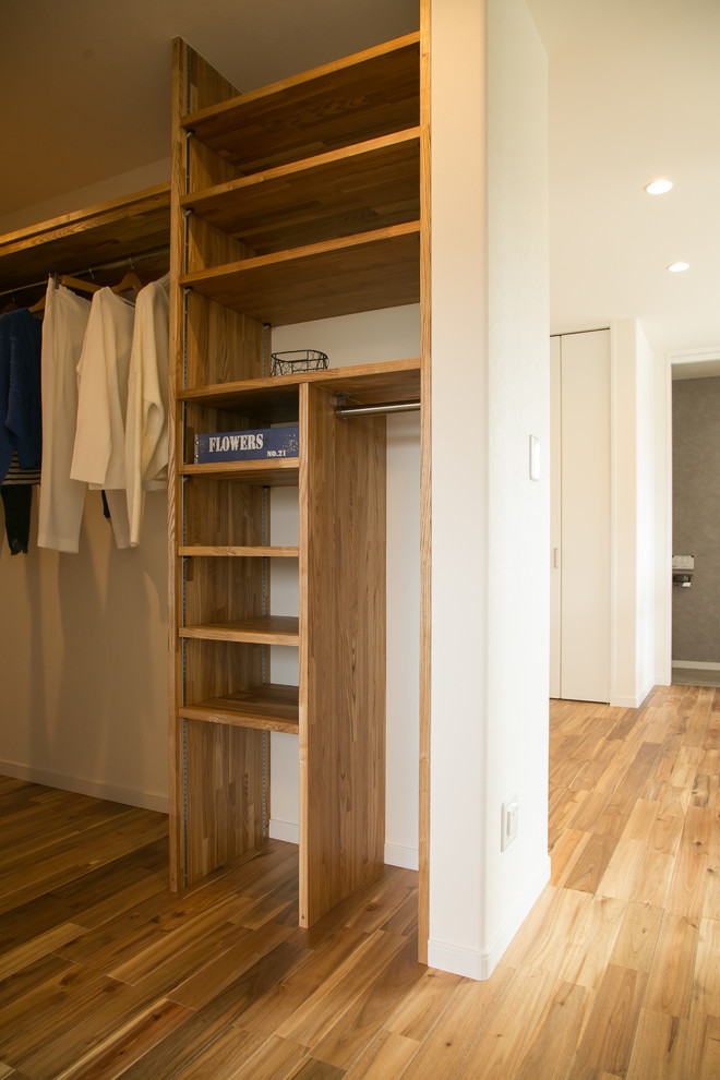 Example of a minimalist gender-neutral medium tone wood floor and brown floor walk-in closet design in Other