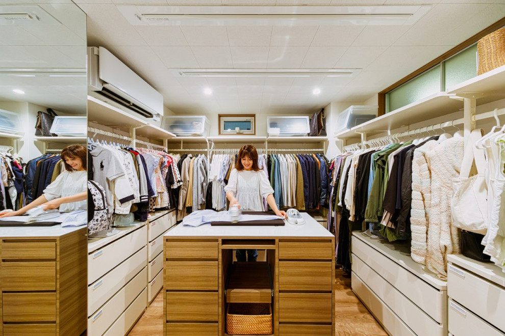 Imagen de armario vestidor unisex actual de tamaño medio con suelo de madera en tonos medios, suelo marrón, papel pintado, armarios abiertos y puertas de armario blancas
