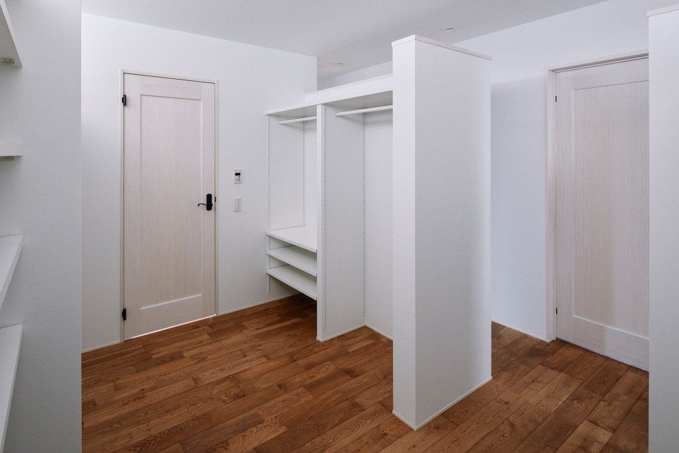 Skandinavisk inredning av ett walk-in-closet för könsneutrala, med öppna hyllor, vita skåp och mörkt trägolv