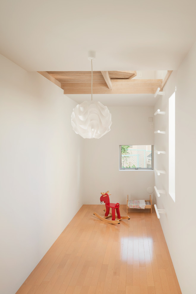 Minimalistisk inredning av ett småbarnsrum kombinerat med lekrum, med vita väggar, ljust trägolv och beiget golv