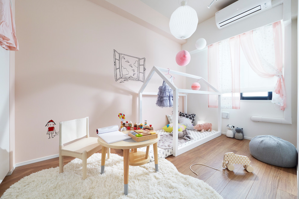 Aménagement d'une chambre d'enfant scandinave avec un mur rose et un sol en bois brun.