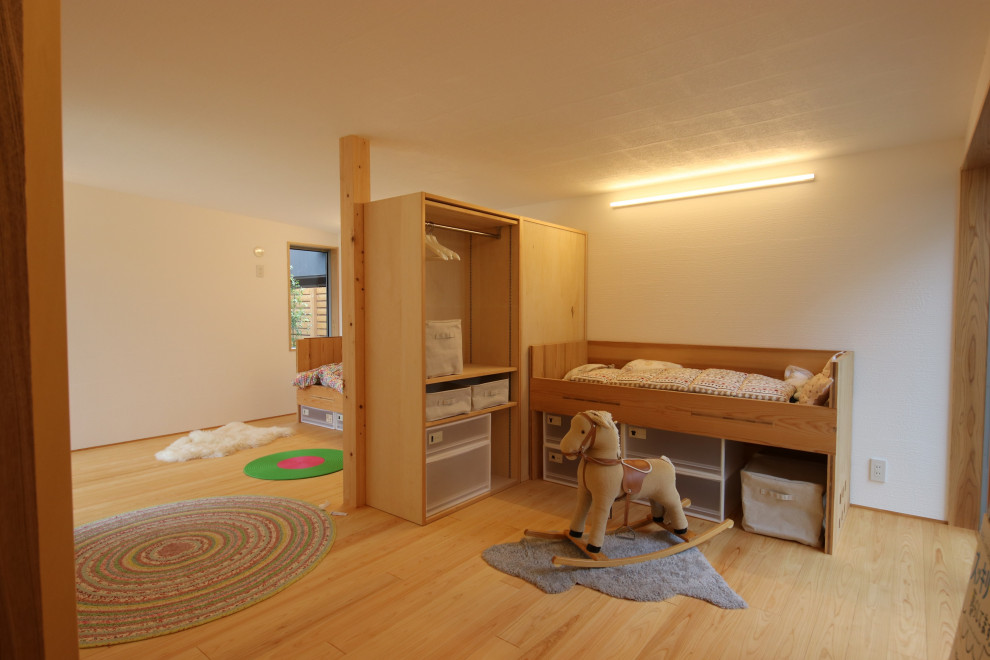 Foto di una piccola cameretta neutra da 1 a 3 anni etnica con pareti bianche e pavimento in legno massello medio