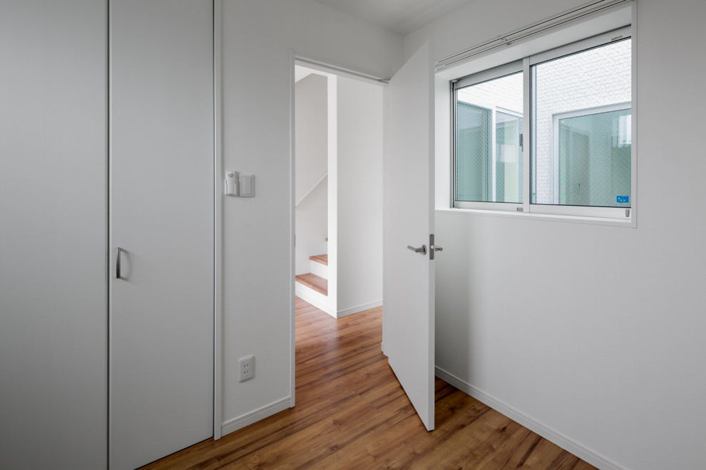 Cette image montre une chambre neutre minimaliste de taille moyenne avec un bureau, un mur blanc, un sol en bois brun, un sol marron, un plafond en papier peint et du papier peint.