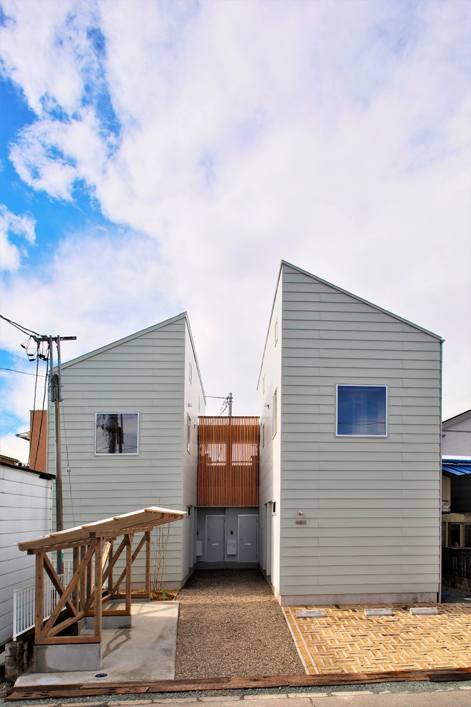 На фото: маленький, двухэтажный, белый многоквартирный дом в восточном стиле с облицовкой из металла, односкатной крышей и металлической крышей для на участке и в саду
