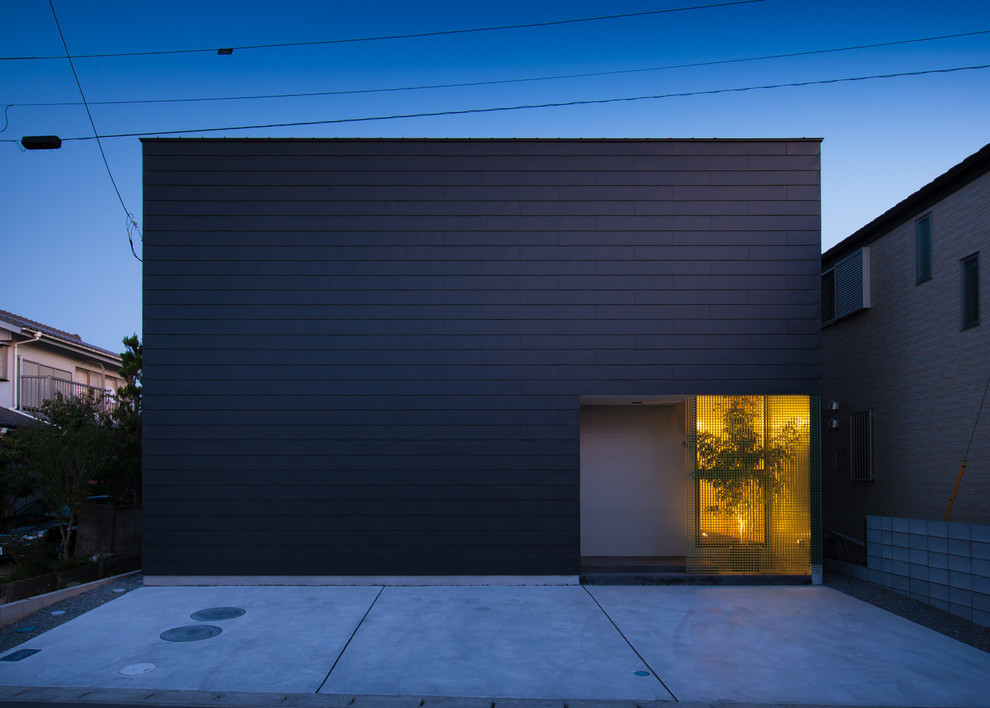 Aménagement d'une façade de maison métallique et noire moderne en bardage à clin de taille moyenne et à un étage avec un toit plat, un toit en métal et un toit noir.