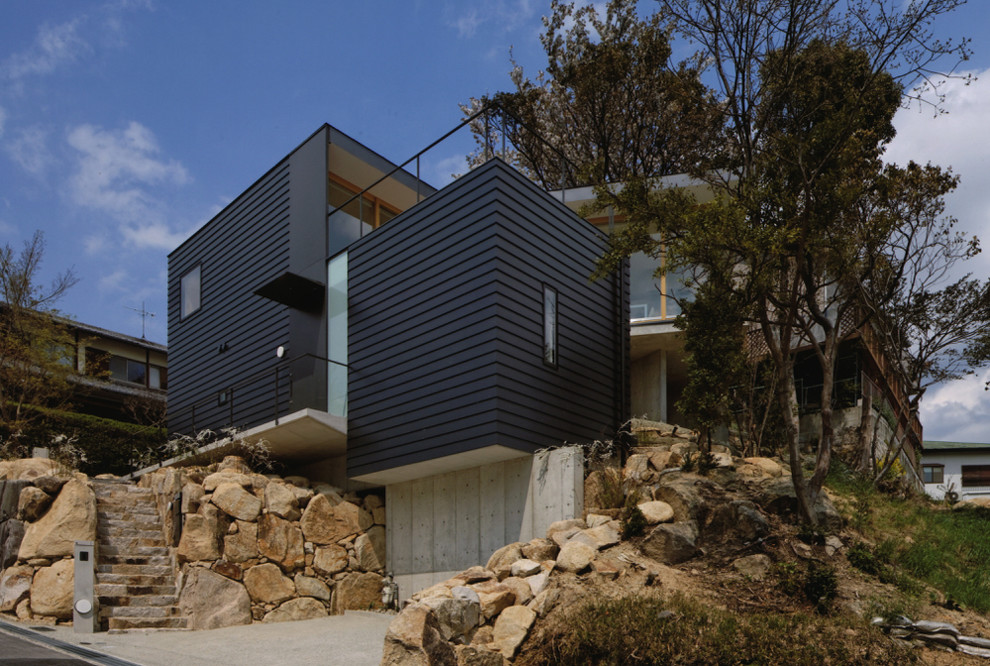 Modelo de fachada de casa azul minimalista de tamaño medio a niveles con revestimiento de aglomerado de cemento, tejado plano y tejado de metal