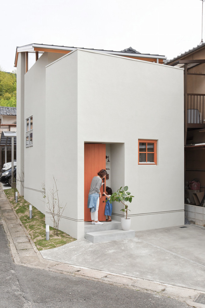 На фото: маленький, двухэтажный, серый частный загородный дом в скандинавском стиле с облицовкой из бетона, полувальмовой крышей и металлической крышей для на участке и в саду