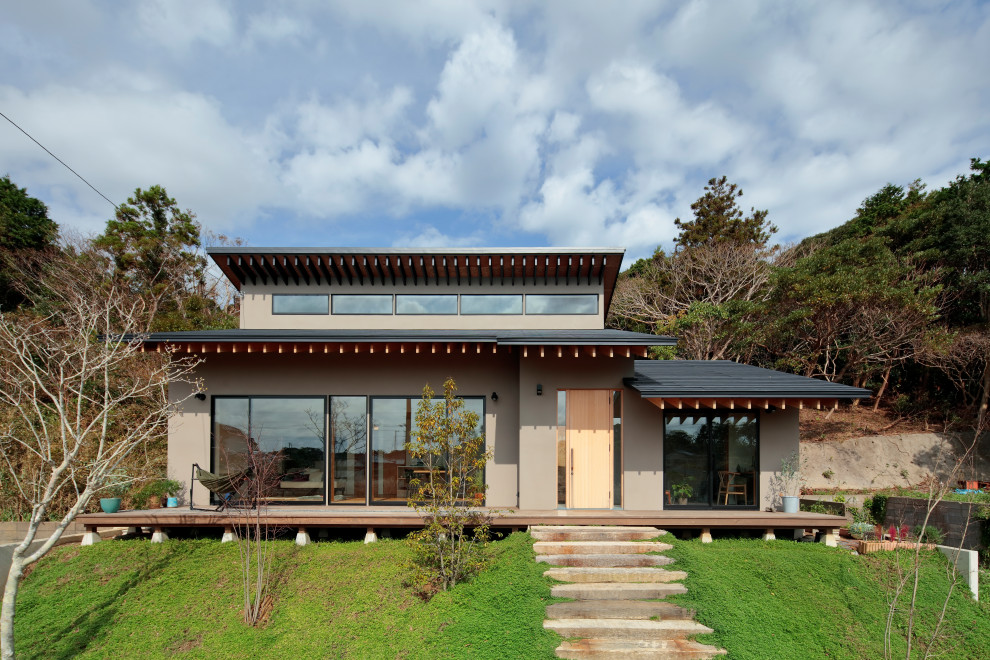 Cette photo montre une façade de maison grise asiatique de plain-pied avec un toit en appentis et un toit noir.