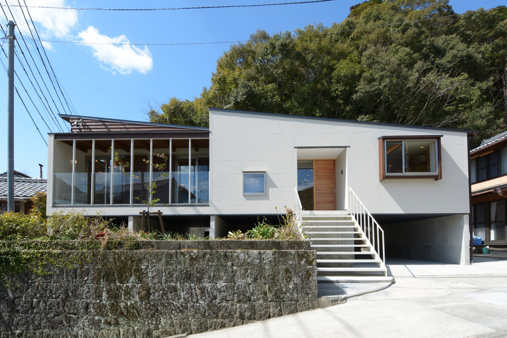 На фото: одноэтажный, белый частный загородный дом в стиле модернизм с облицовкой из бетона и односкатной крышей