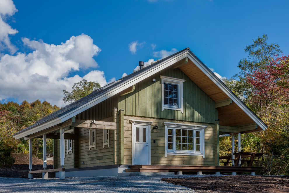 Photo of a green farmhouse house exterior in Other with wood cladding and a pitched roof.