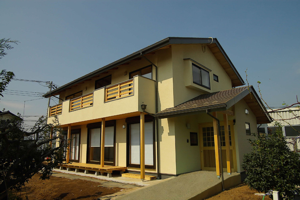 Ejemplo de fachada de casa amarilla de estilo zen grande de dos plantas con revestimiento de estuco, tejado a dos aguas y tejado de metal