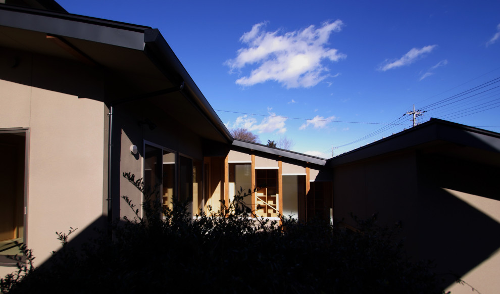 Réalisation d'une façade de maison marron minimaliste en stuc de taille moyenne et à un étage avec un toit à deux pans et un toit en métal.