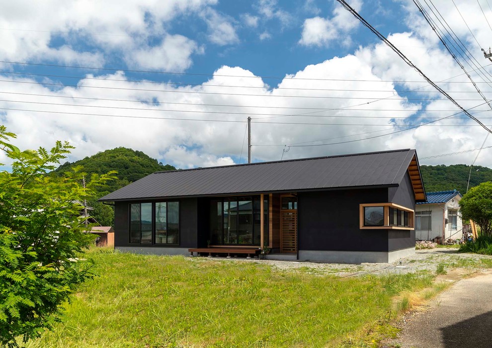 Cette image montre une façade de maison noire asiatique en stuc de taille moyenne et de plain-pied avec un toit à deux pans et un toit en métal.