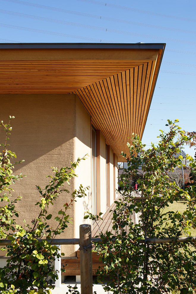 Idées déco pour une façade de maison beige asiatique en stuc de taille moyenne et de plain-pied avec un toit à quatre pans et un toit en métal.