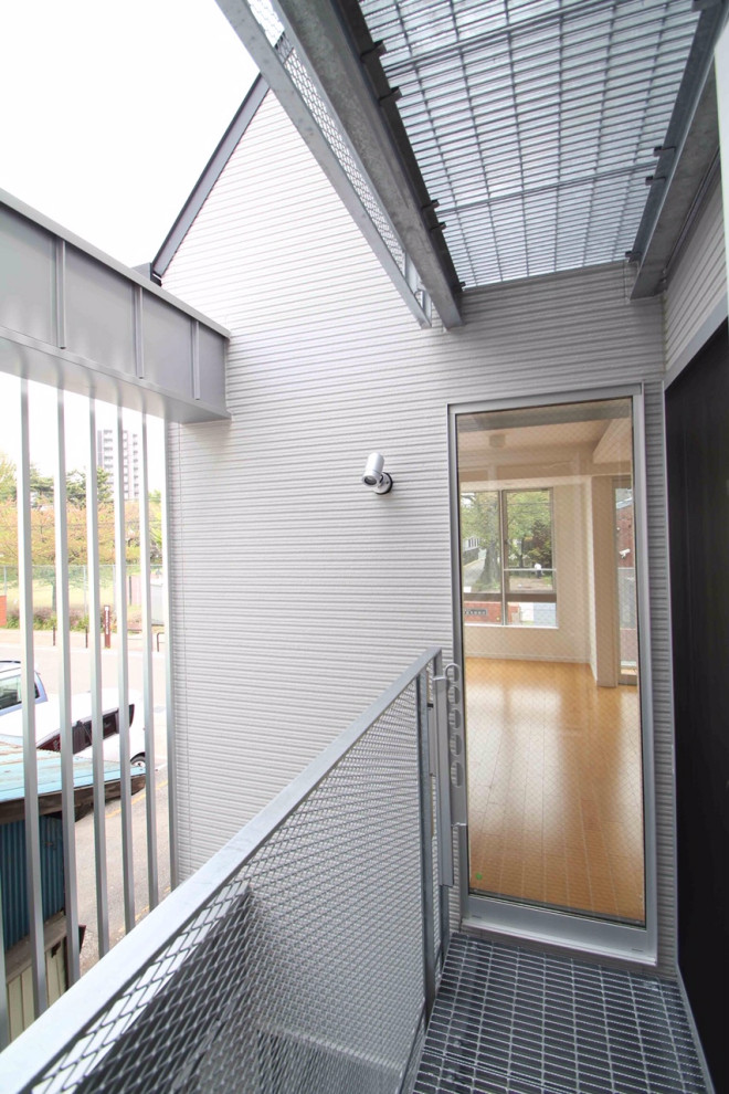 Imagen de fachada de casa gris minimalista de tamaño medio de tres plantas con revestimiento de estuco, tejado plano y tejado de varios materiales