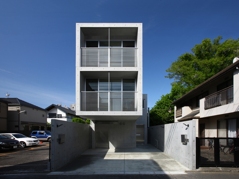 Gey modern concrete detached house in Tokyo with three floors and a flat roof.