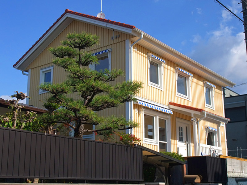 Modelo de fachada de casa amarilla escandinava de tamaño medio de dos plantas con revestimiento de madera, tejado a dos aguas y tejado de teja de barro