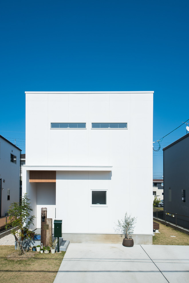 Foto på ett minimalistiskt vitt hus, med två våningar, pulpettak och tak i metall