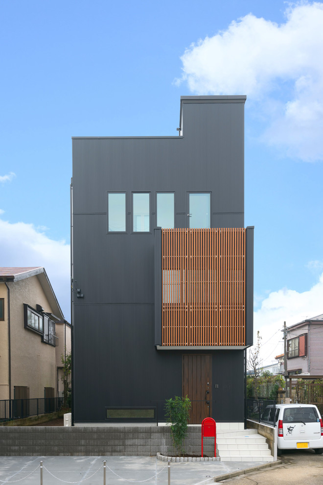 Imagen de fachada de casa negra bohemia de tres plantas con revestimiento de metal y tejado plano