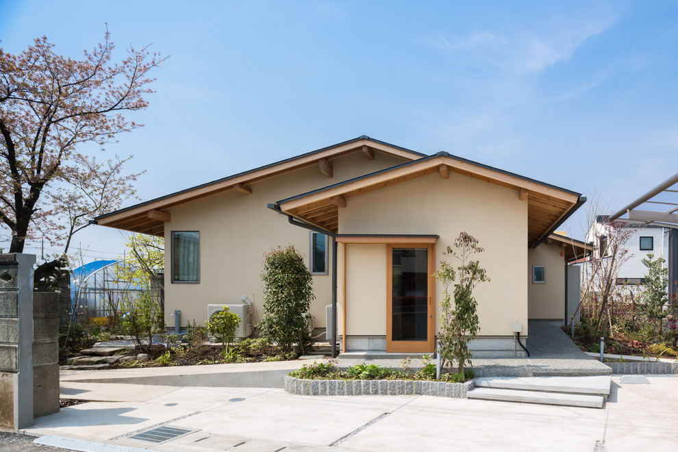 Aménagement d'une façade de maison beige asiatique avec un toit à deux pans.