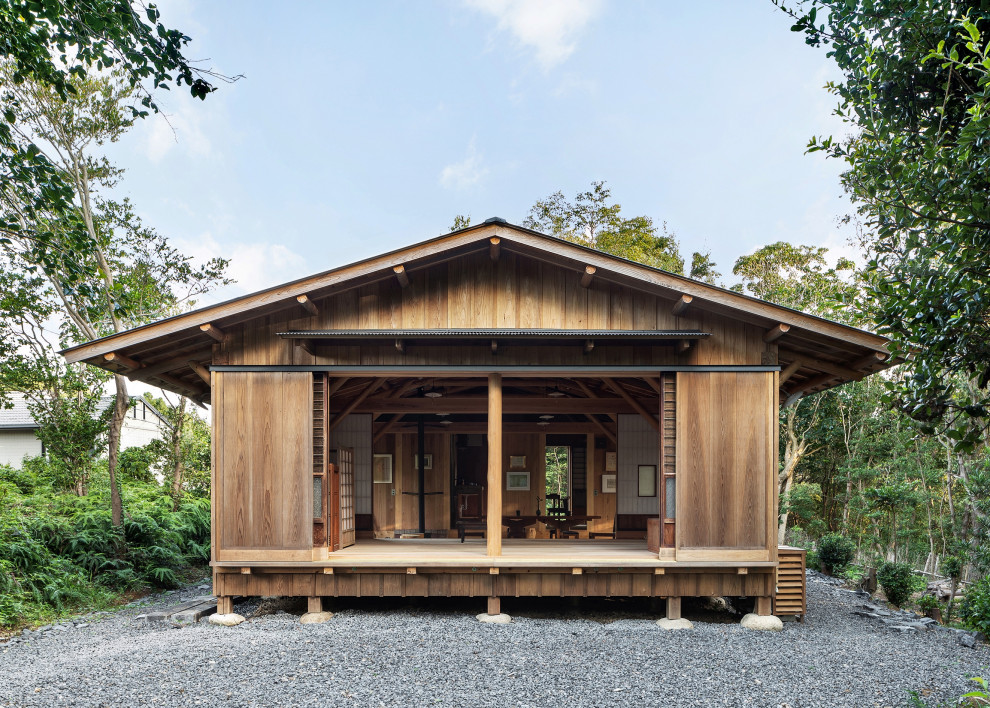 Cette image montre une grande façade de maison marron asiatique en bois de plain-pied avec un toit à deux pans, un toit en métal et un toit gris.