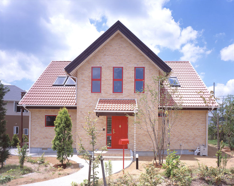 Réalisation d'une façade de maison beige nordique en brique à un étage avec un toit à deux pans et un toit en tuile.