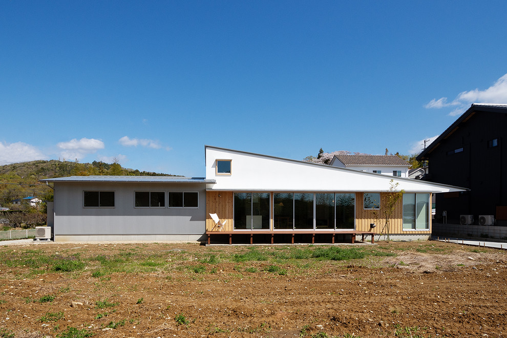 Aménagement d'une grande façade de maison blanche scandinave en planches et couvre-joints de plain-pied avec un revêtement mixte, un toit en appentis, un toit en métal et un toit gris.