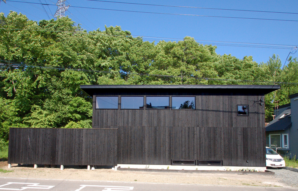 Idée de décoration pour une petite façade de maison noire minimaliste en bois à un étage avec un toit plat et un toit en métal.