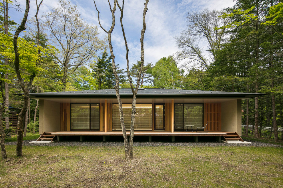 Cette image montre une façade de maison beige asiatique en bois de plain-pied avec un toit à quatre pans et un toit en métal.