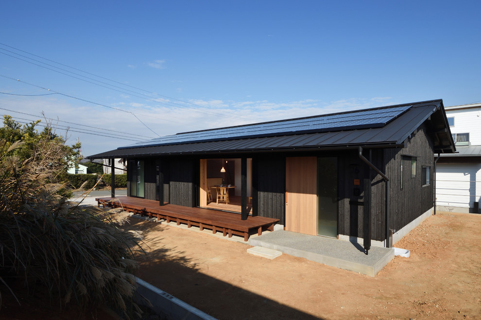 Cette image montre une façade de maison noire minimaliste en bois de plain-pied avec un toit à deux pans et un toit en métal.