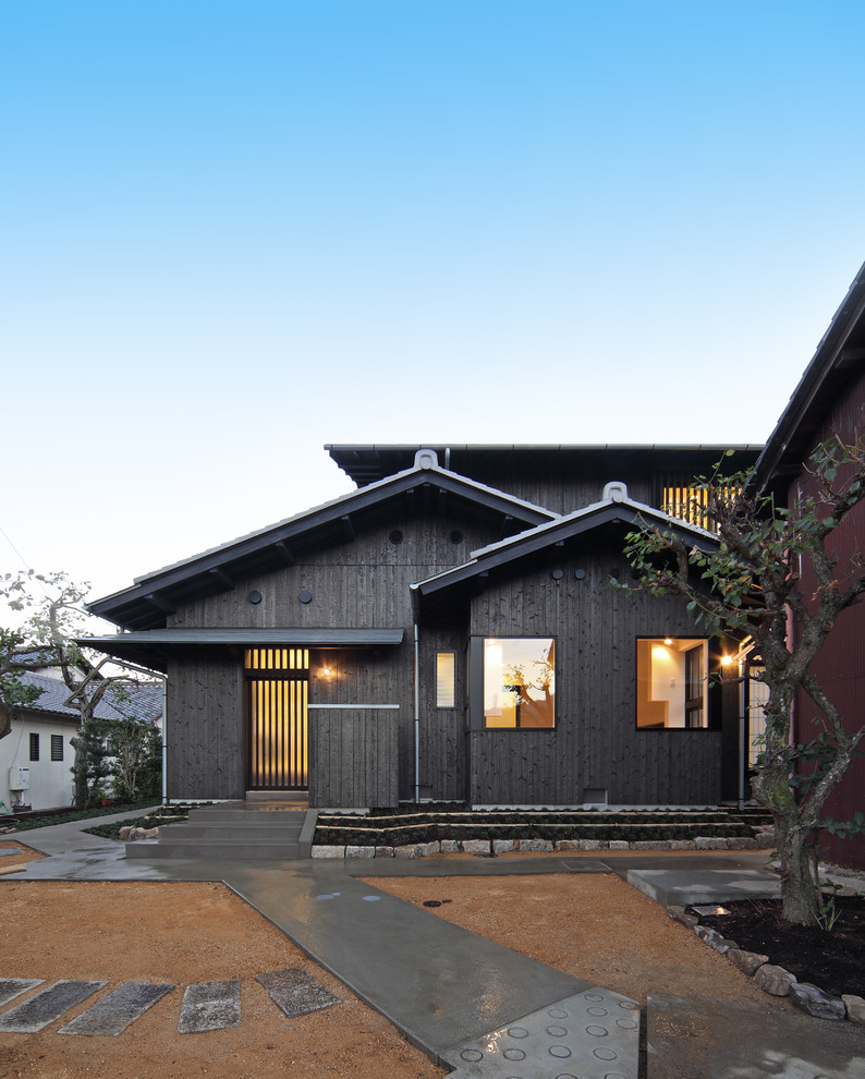 Diseño de fachada de casa negra asiática de tamaño medio de dos plantas con revestimiento de madera, tejado a dos aguas y tejado de metal