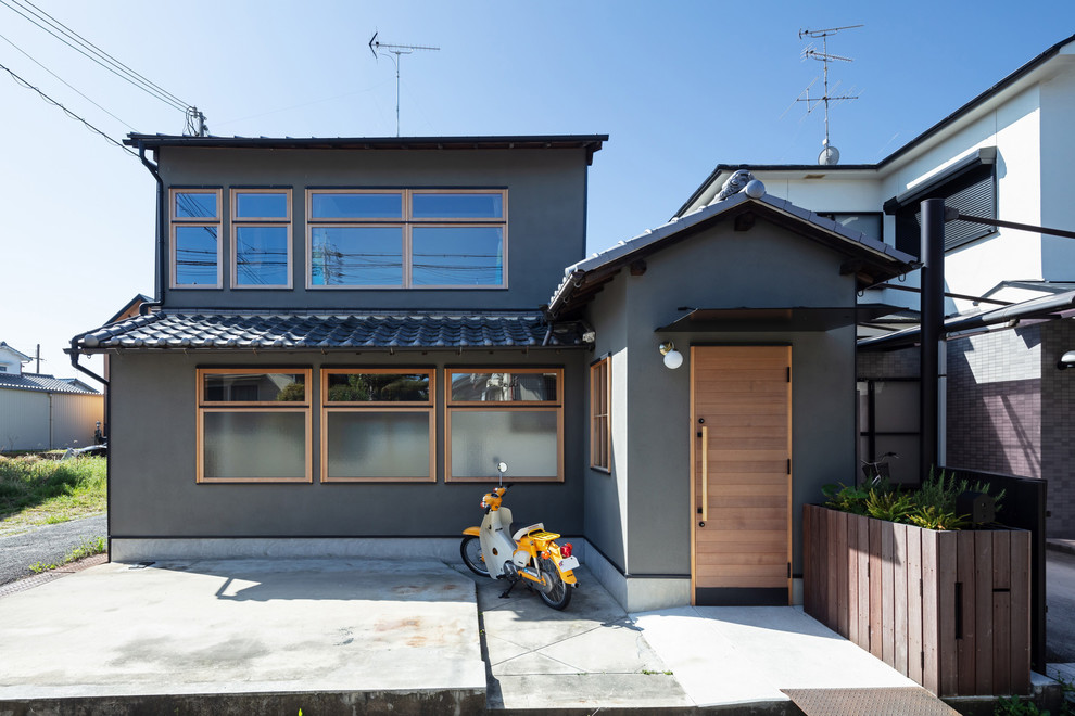 Ejemplo de fachada de casa gris asiática de tamaño medio de dos plantas con revestimiento de estuco, tejado a dos aguas y tejado de varios materiales
