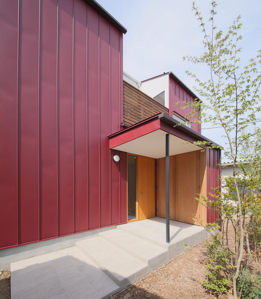 Foto på ett mellanstort funkis rött hus, med två våningar, metallfasad, sadeltak och tak i metall