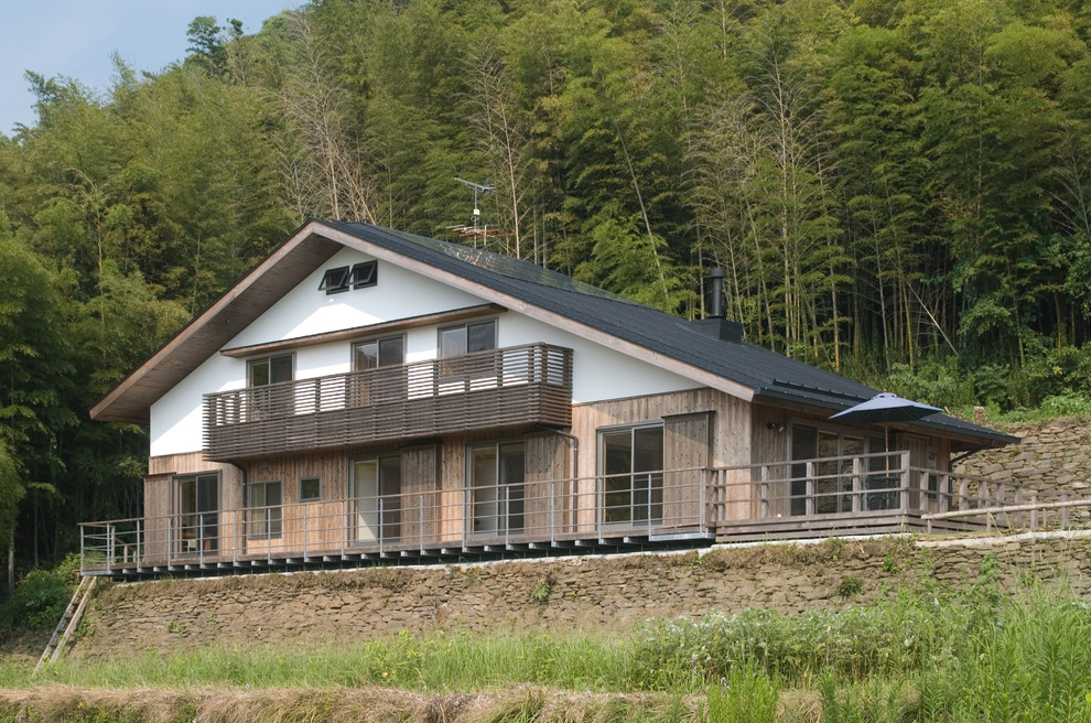Imagen de fachada de casa marrón asiática de dos plantas con revestimiento de madera, tejado a dos aguas y tejado de varios materiales