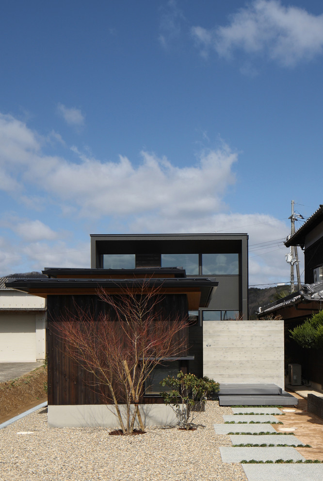 Modelo de fachada de casa negra de estilo zen grande de dos plantas con revestimiento de madera, tejado a cuatro aguas y tejado de metal